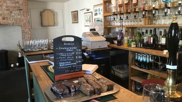 Bar counter with a variety of drinks, glassware, a chalkboard menu, and a platter of snacks in a cozy setting.