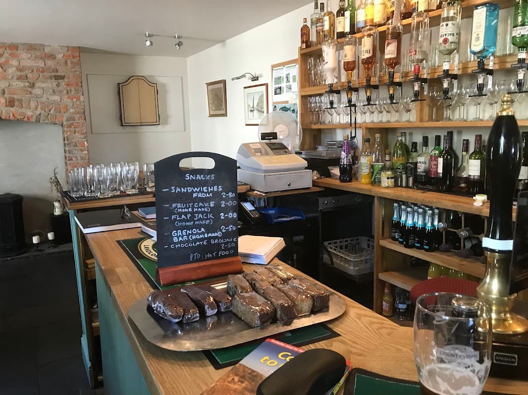Bar counter with a variety of drinks, glassware, a chalkboard menu, and a platter of snacks in a cozy setting.