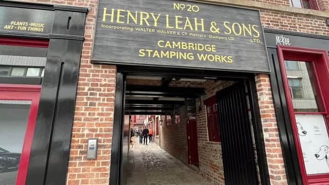 Brick archway entrance with a wooden sign for "Henry Leah & Sons" and people walking through Leah's Yard in Sheffield.