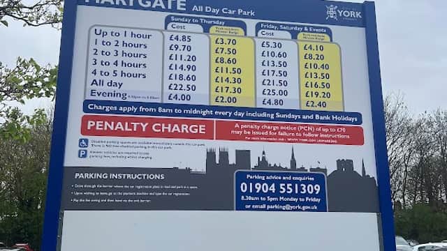 Sign displaying parking rates and instructions at Marygate Car Park, York, with cars parked in the background.