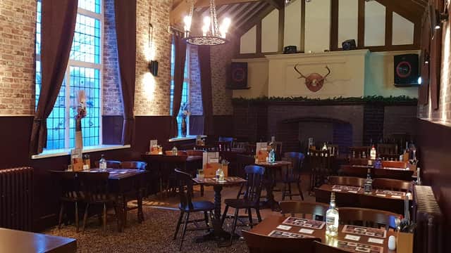 Rustic dining area with wooden tables, chairs, a stone fireplace, and large windows, featuring warm lighting and decor.