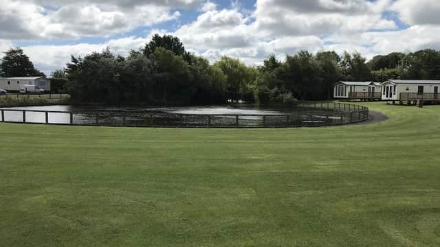 A serene caravan park with a pond, surrounded by greenery and holiday homes under a cloudy sky.