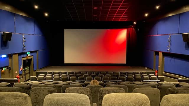 Interior of a theater with plush gray seating, a large screen, and blue walls, illuminated by soft red lighting.