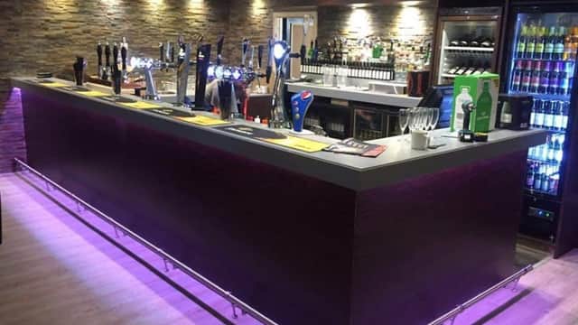 Modern bar with a sleek counter, illuminated taps, and shelves stocked with drinks in a cozy setting.