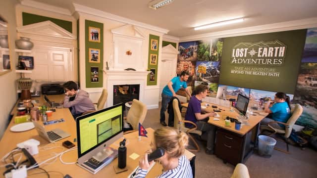 Office scene at Lost Earth Adventures with staff at desks, engaging in calls, and adventure-themed wall decor.