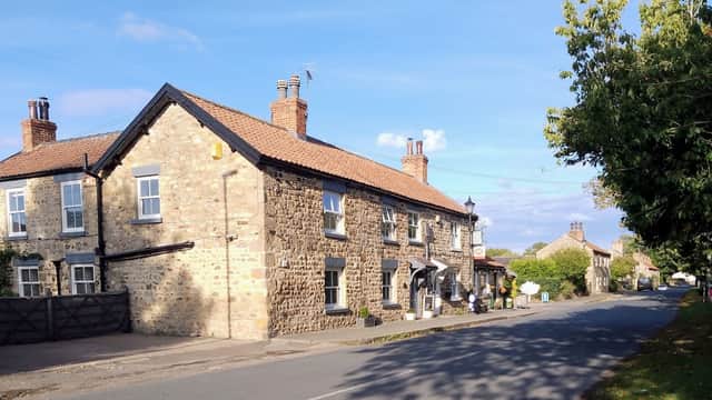 Stone building with a tiled roof, surrounded by trees, along a quiet road in West Tanfield, Yorkshire.