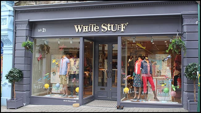 Clothing shop front with mannequins in colorful outfits, large windows, and playful decor elements.