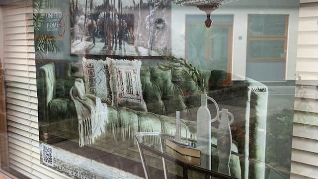 A stylish display featuring a green sofa, decorative pillows, and a chandelier in a window setting.