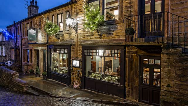 Historic stone building with festive lights, large windows revealing a cozy restaurant interior on a cobblestone street.