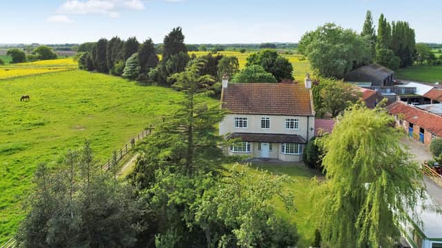Aerial view of a house surrounded by greenery, fields, and trees, with horses grazing in the distance.
