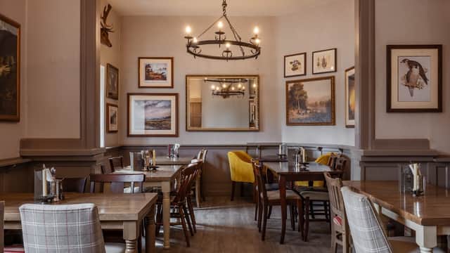 Cozy restaurant interior with wooden tables, chairs, framed artwork, and a chandelier in a welcoming atmosphere.