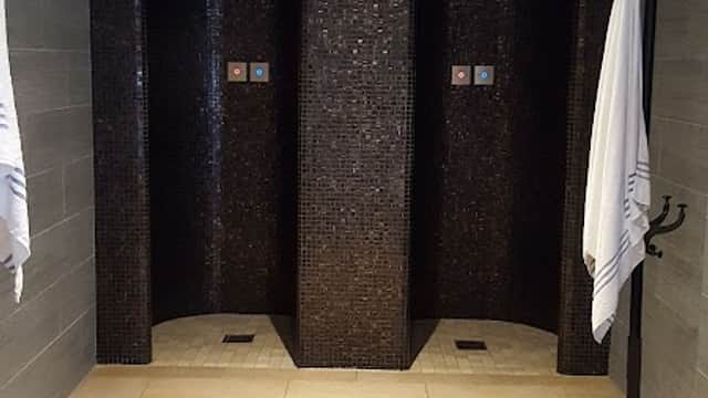 Luxurious shower area with dark tiled walls, two shower stalls, and hooks for towels on a stone floor.