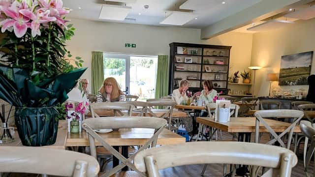 Bright café interior with wooden tables, floral arrangements, and patrons enjoying meals in a cozy atmosphere.