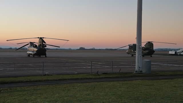 Two military helicopters parked on an airstrip at dawn, with a soft pastel sky in the background.