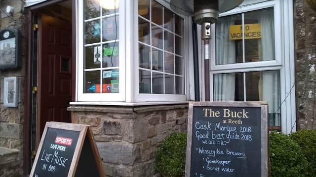 The Buck bar entrance with outdoor seating, menu board, and signs for live music and local breweries.