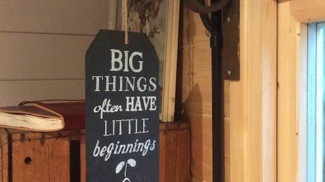 Chalkboard sign reading "BIG THINGS often HAVE little beginnings" hangs from a rustic shelf in a cozy flower shop.