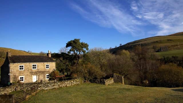 Stone building surrounded by trees and hills under a blue sky in Keld, Yorkshire.