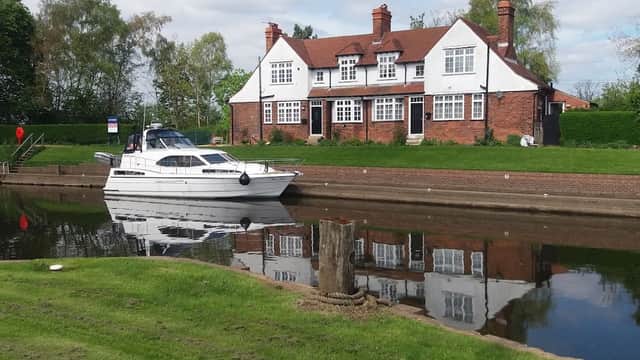 A white boat is moored beside a red-brick building with multiple windows, reflected in the calm water of the canal.