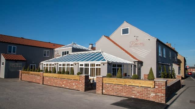 Quaint restaurant with a glass conservatory, surrounded by neatly trimmed hedges and a clear blue sky.