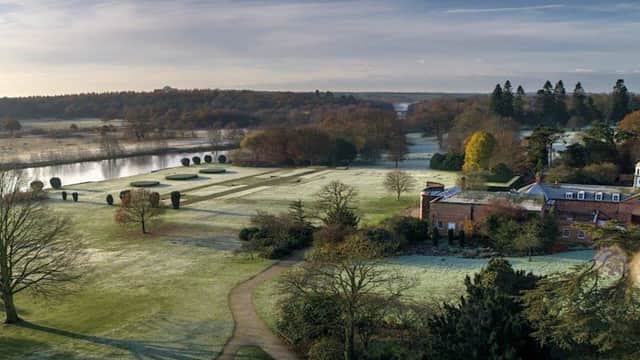 Expansive parkland with frosted grass, a winding path, a lake, and a historic brick building surrounded by trees.