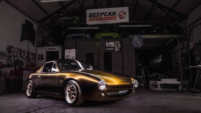 A sleek golden sports car with custom wheels inside a workshop, featuring tools and car parts in the background.
