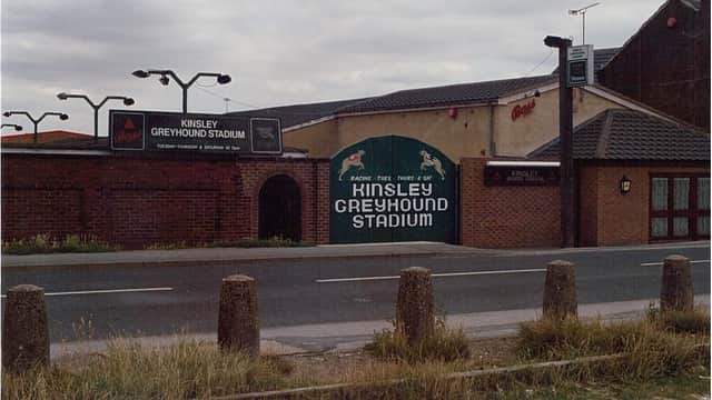 Kinsley Greyhound Stadium entrance with signage, brick walls, and a road in front. Overcast sky in the background.