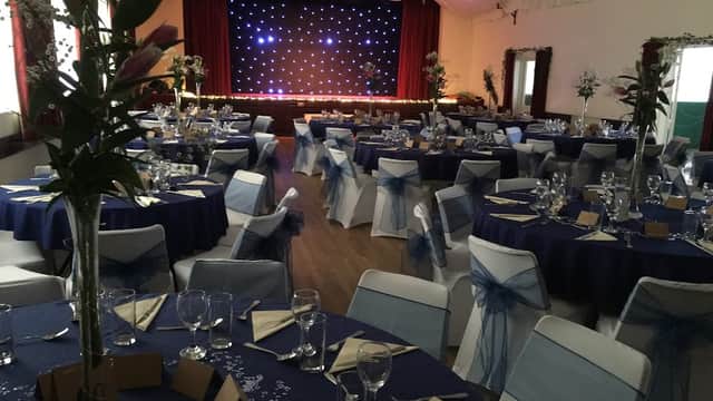 Elegant event space with round tables, blue and white decor, and a stage with twinkling lights in Hampsthwaite Memorial Hall.