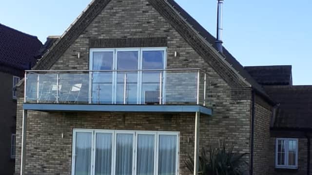 Modern brick house with a balcony, large windows, and green lawn under a clear blue sky.
