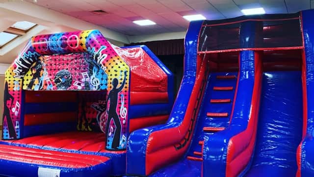 Colorful inflatable bouncy castle and slide in a spacious indoor hall with bright lighting.