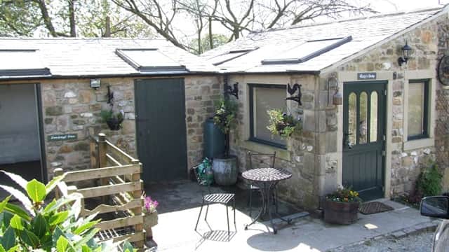 Charming stone cottage with a green door, outdoor seating, and flower pots in a rural setting.