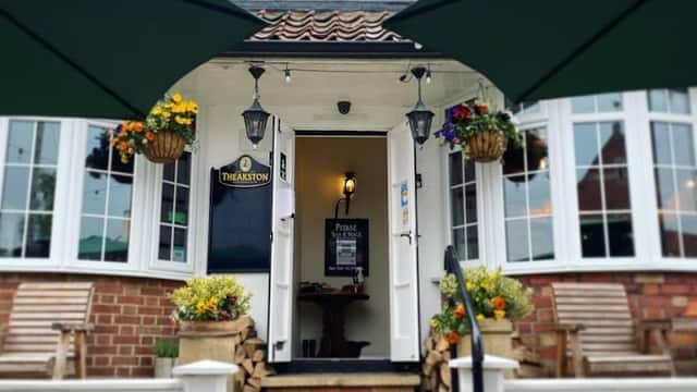 Charming pub entrance with green awnings, flower baskets, and wooden seating in Raskelf, Yorkshire.