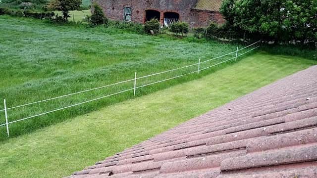 View from a roof showing a grassy field, a rustic building, and trees under a cloudy sky in Bempton, Yorkshire.