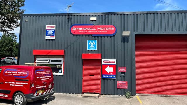 Springwell Motors building with red signage, a reception area, and a service van parked outside under a clear blue sky.