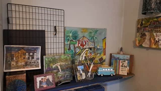 Colorful artwork and framed photos displayed on a shelf, with a blue radiator beneath in a cozy interior setting.
