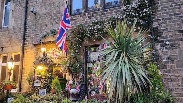 Charming hotel with British flags, greenery, and flower pots, set in a stone building in Oxenhope, Yorkshire.