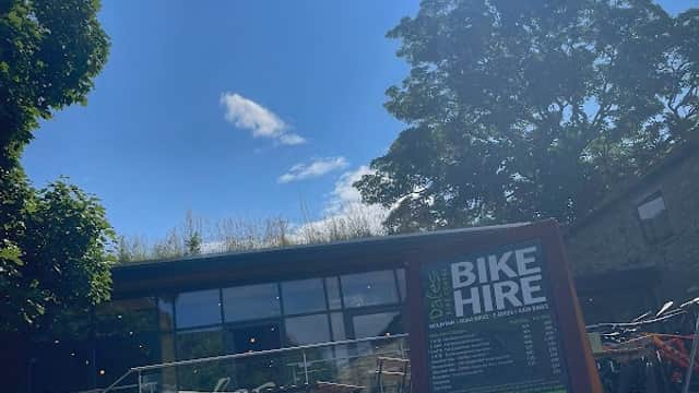 Sunny day at Dales Bike Centre with a bike hire sign and outdoor seating in front of a stone building.