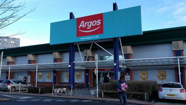 Argos store entrance with large sign, shoppers, and parked cars outside in Leeds, Yorkshire.