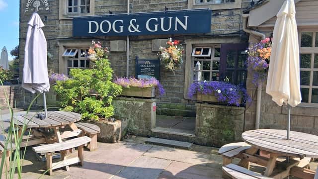 Quaint restaurant exterior with "DOG & GUN" sign, flower pots, outdoor seating, and umbrellas in Sutton-in-Craven.