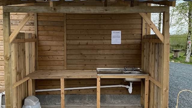 Wooden shelter with a countertop and sink, surrounded by gravel and potted plants, at Elm Lodge Holiday Park.