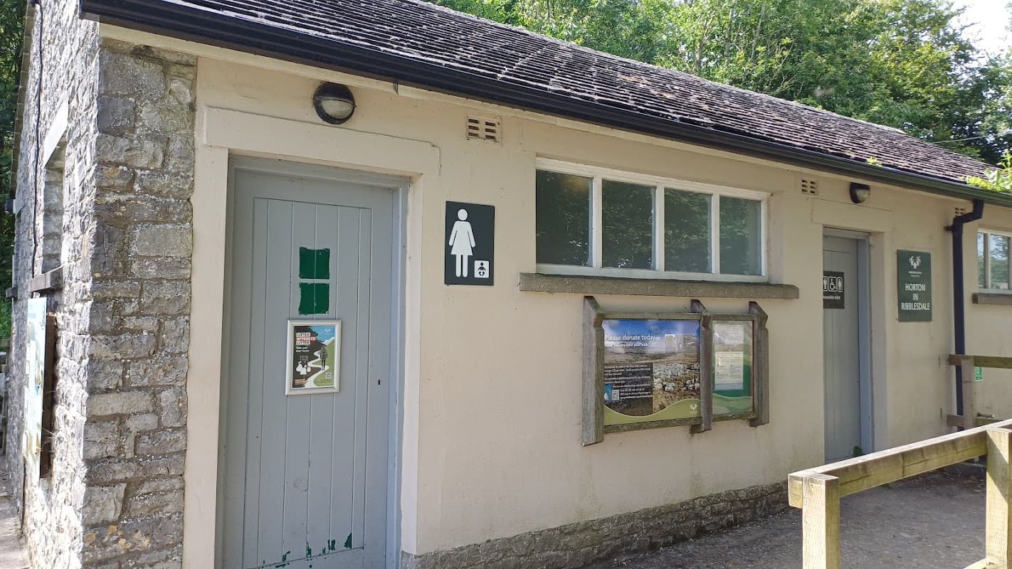 Public toilets building with signs for men's and women's facilities, surrounded by greenery in Horton-in-Ribblesdale.