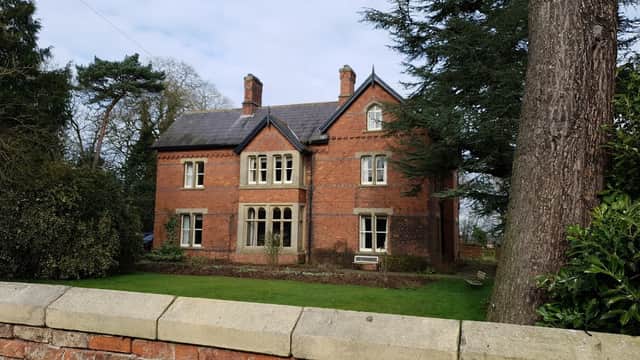 Victorian-style brick building with large windows, surrounded by greenery and a stone wall in Little Ouseburn.
