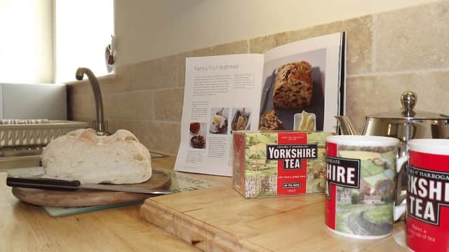 Freshly baked bread on a wooden board, with Yorkshire tea and a recipe book in a cozy kitchen setting.