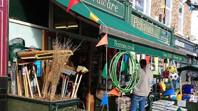 Pextons Hardware storefront with colorful bunting, garden tools, and various supplies displayed outside.