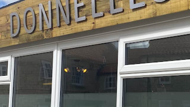 Sign for Donnelles Hair Studio with large letters, windows reflecting a blue sky, and a brick wall below.
