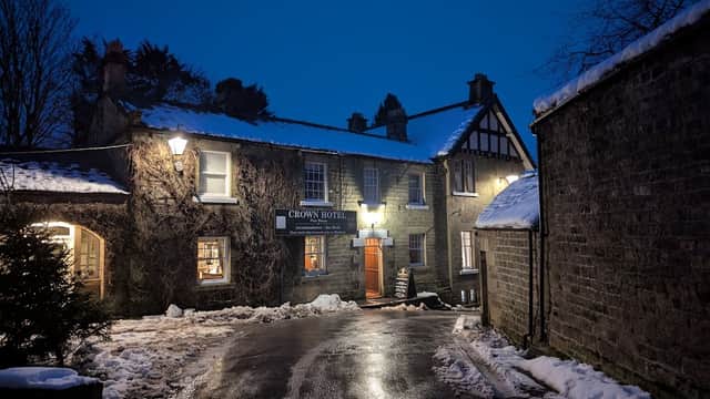 Crown Hotel in Lofthouse, North Yorkshire, with snow-covered ground and warm lights illuminating the entrance at dusk.