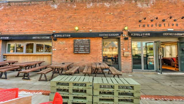 Outdoor seating area with wooden benches, a bar entrance, and a brick wall featuring the "Revolution" sign.