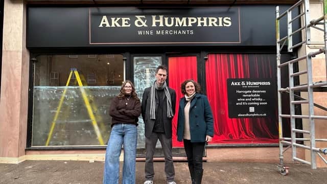 Ake & Humphris Wine Bar & Shop storefront with three people standing in front, scaffolding, and a red curtain backdrop.