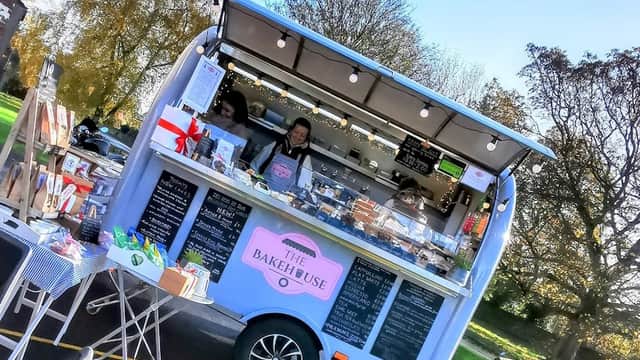 A vibrant food truck with "The Bakehouse" sign serving baked goods, surrounded by trees and clear blue skies.