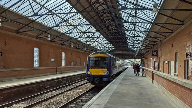 Train arriving at Beverley Railway Station, featuring a brick platform, large windows, and a metal roof structure.