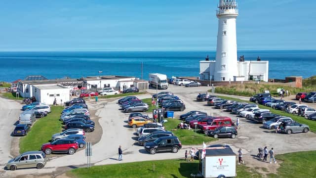 Lighthouse beside a busy car park with numerous vehicles and visitors, overlooking the sea at Flamborough Head.